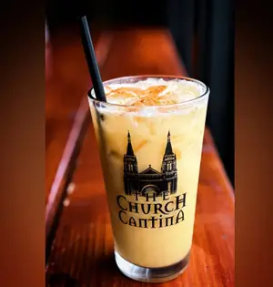 A tall iced pumpkin drink with cinnamon on top, in a Church Cantina pint glass with a black straw