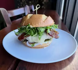 A fried chicken sandwich with lettuce, bacon and melted cheese on a Hawaiian bun