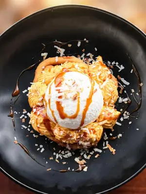 Pumpkin pie funnel cake topped with vanilla ice cream, toasted coconut and caramel, on a black plate