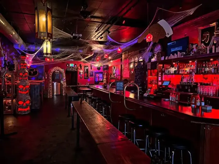 Inside The Church Cantina: a long wooden bar lit red, cobwebs across the ceiling and skulls beside an arched doorway